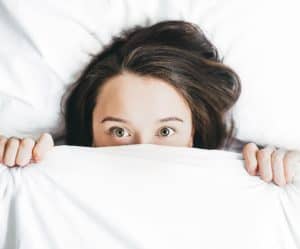 women under bed covers deciding where to go for flu treatment